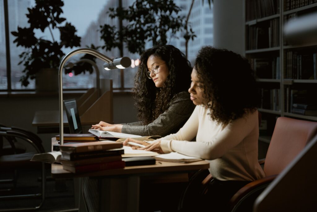 Two woman at the library sitting at a desk 