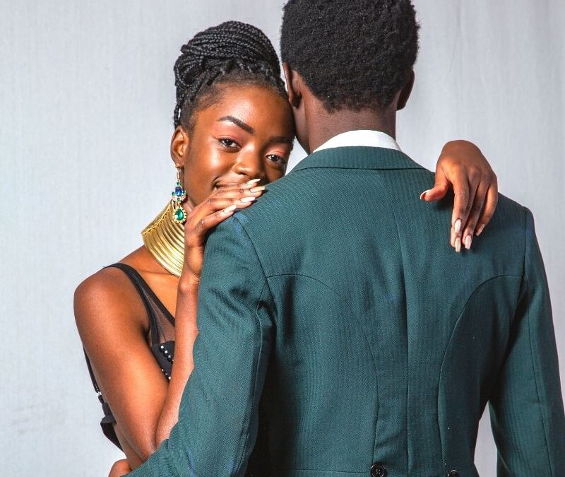 Black man with his back turned in a suit hugging a black women who is smiling