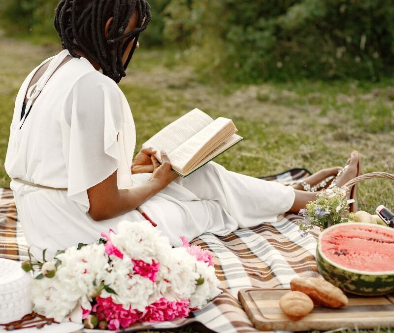 Black Woman Sitting On The Floor At A Picnic reading a book