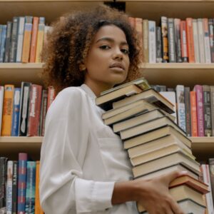 Black girl in the library holding a stack of books 