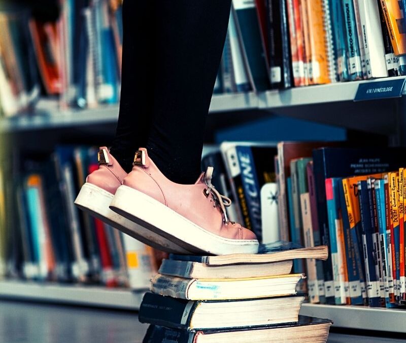 pair of legs standing on a stack of book in library