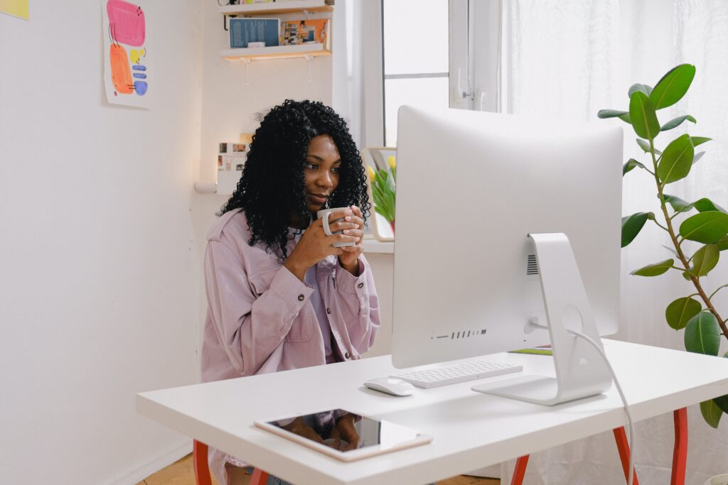 Black woman sitting at a computer desk drinking coffee 