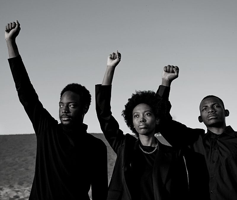 three black people standing with their fists up