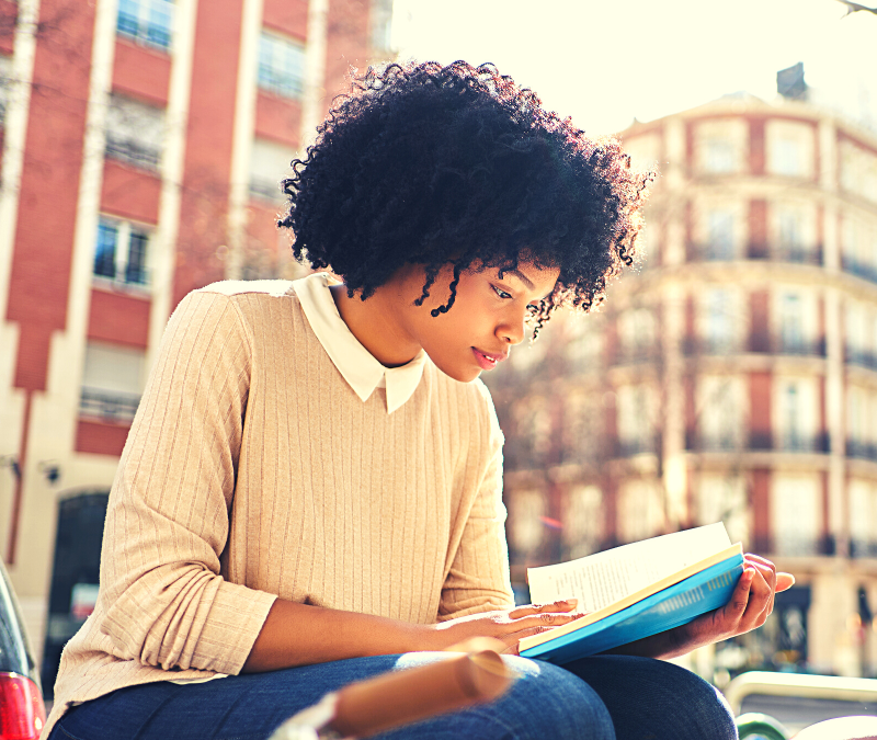 A Black woman sitting outside reading a book